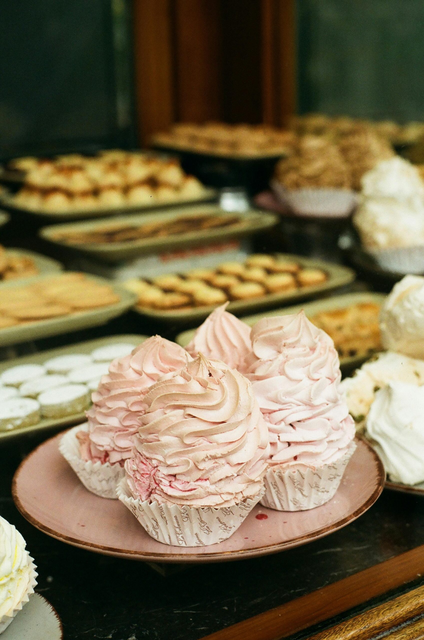 Artistic capture of pink meringue desserts set against a backdrop of assorted pastries.