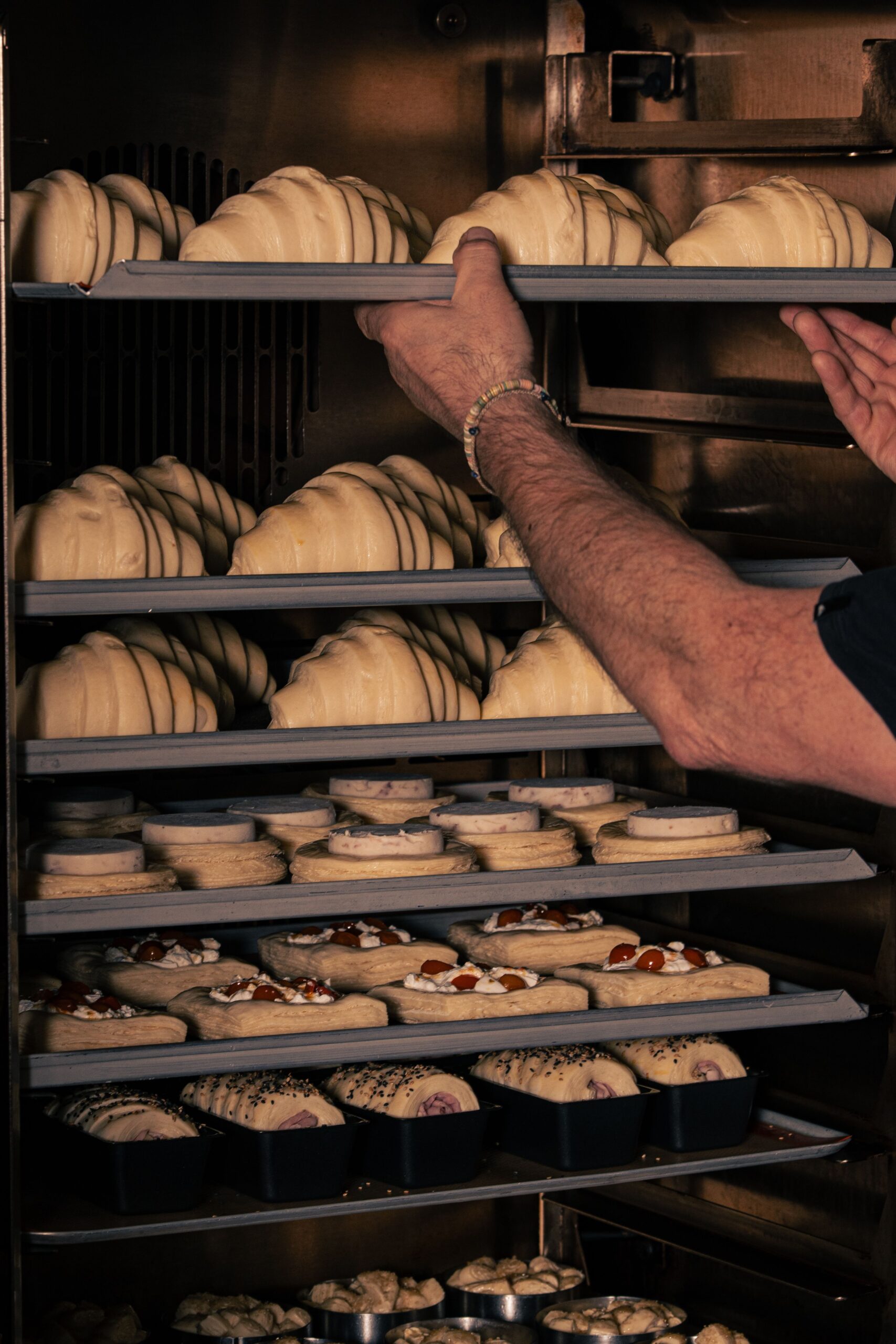 A baker organizing fresh croissants and pastries on trays in a commercial oven, showcasing a busy kitchen environment.